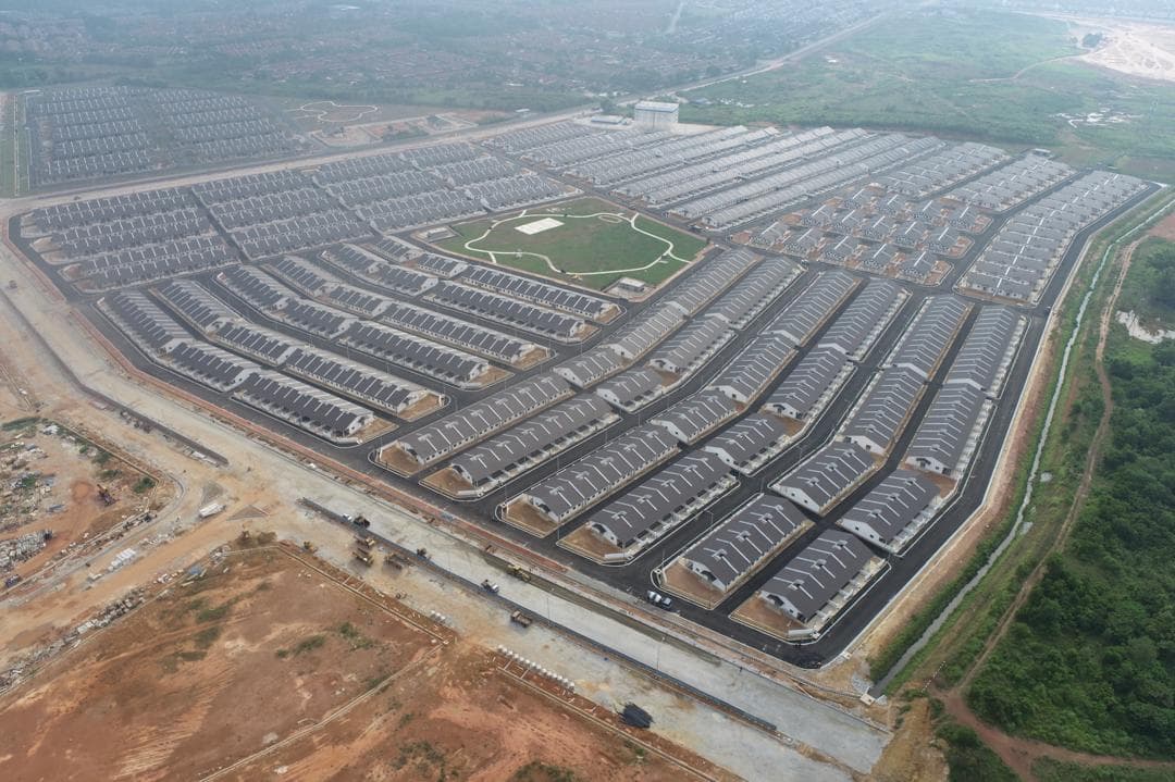 Wide aerial view of extensive dark-roofed housing rows surrounding landscaped green spaces and roads.